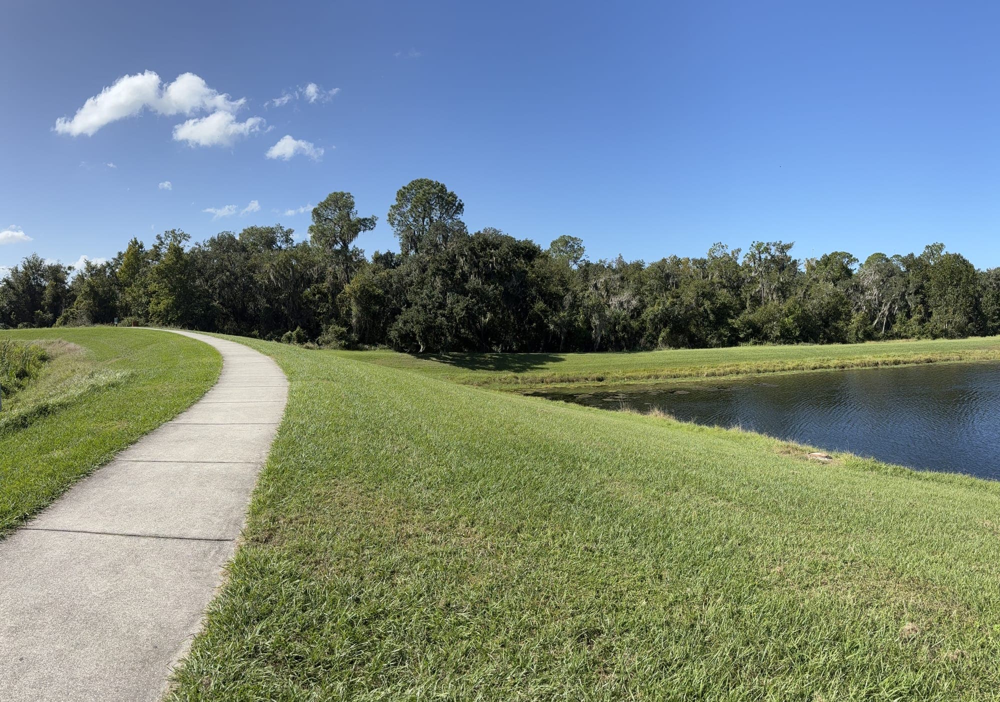 The path curving down the rise with a second pond on the right and clouds overhead.