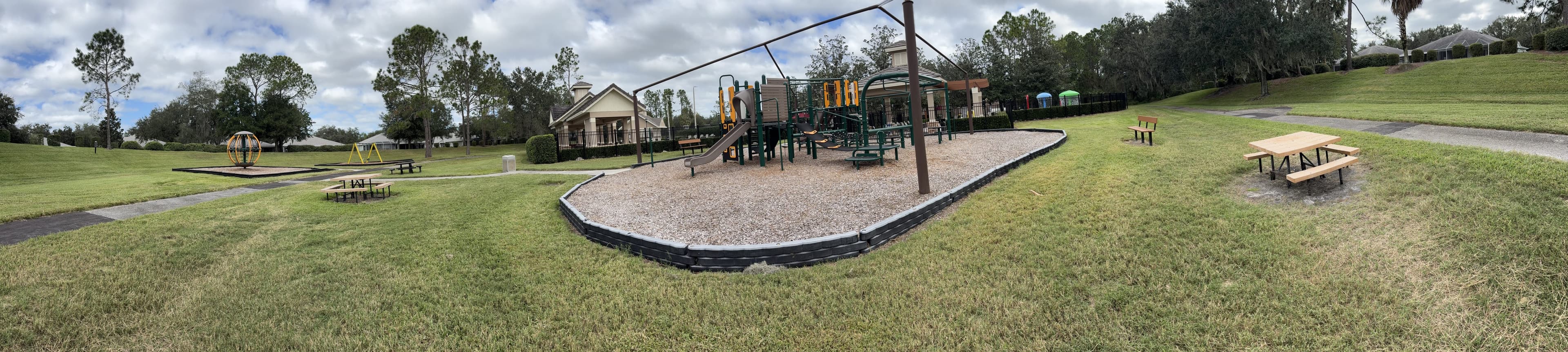 Panorama from the bench: a lawn with picnic tables and swings, the playground in the middle, more picnic tables on the right.