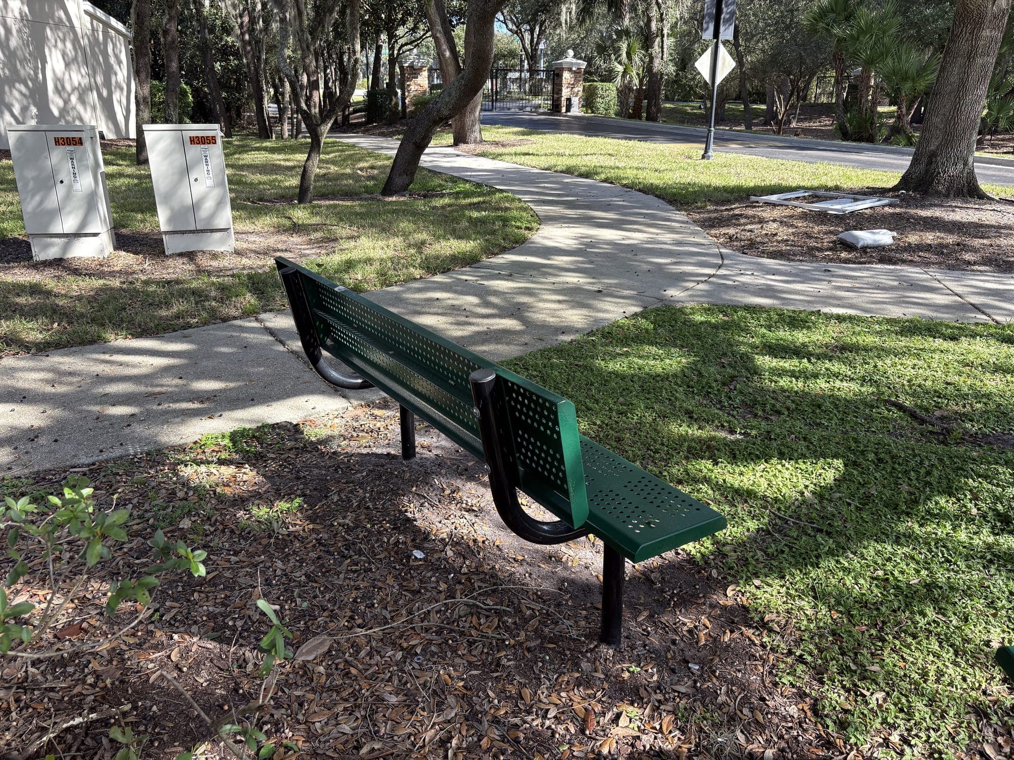 One bench beside the sidewalk, with utility boxes and houses behind it.