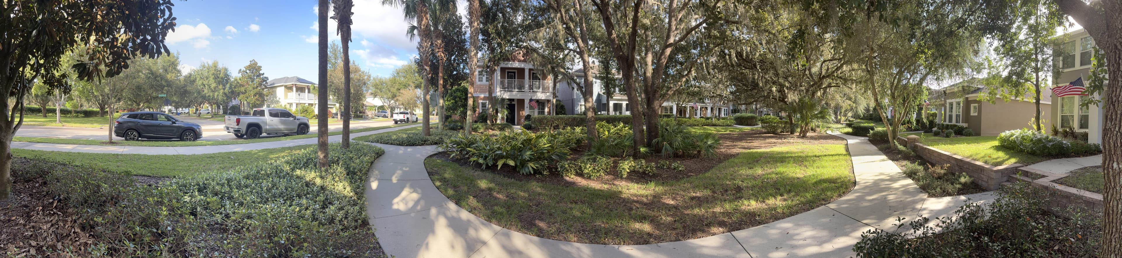Panorama from the bench: a street with parked cars on the left, a garden with a curving path, and houses on the right.
