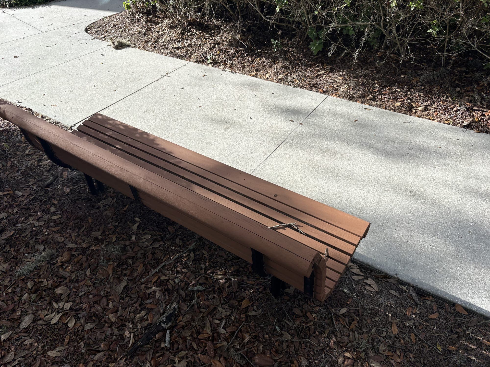 The bench beside a sidewalk, set on mulch under the trees.