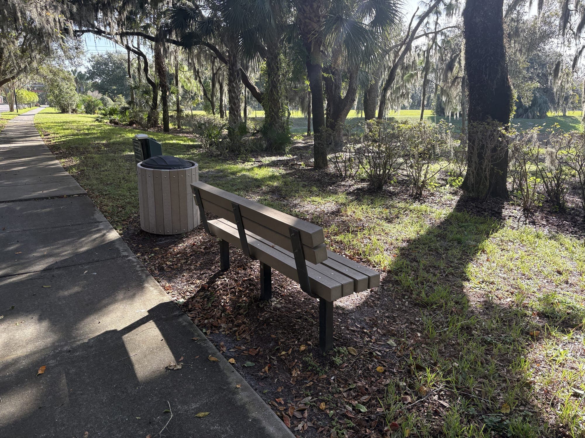 The bench from the other side, with a tan trash can right next to it.