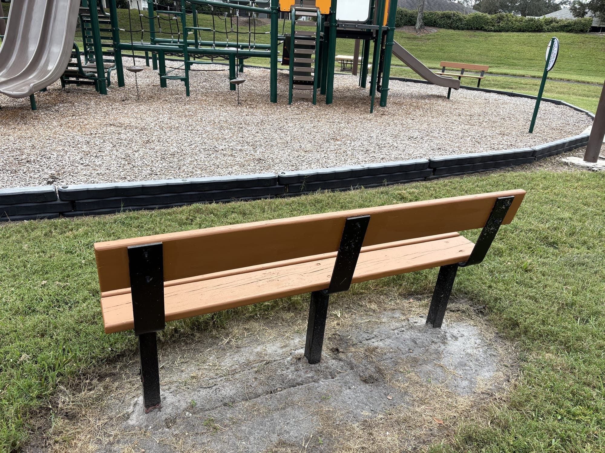 The bench from behind, facing the playground on its bed of gravel.