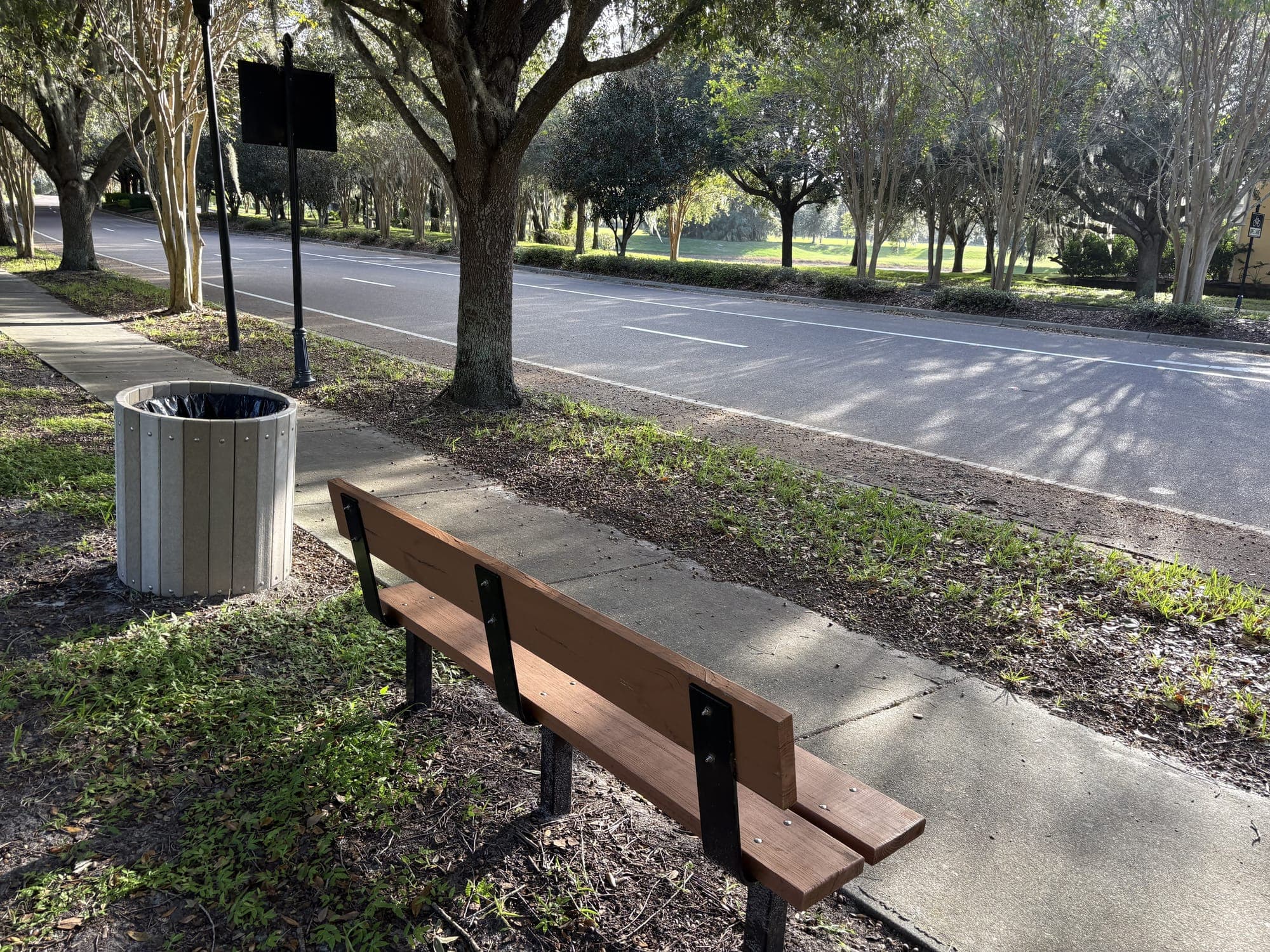 The bench from the side, a trash can, lampposts and a sign behind it.