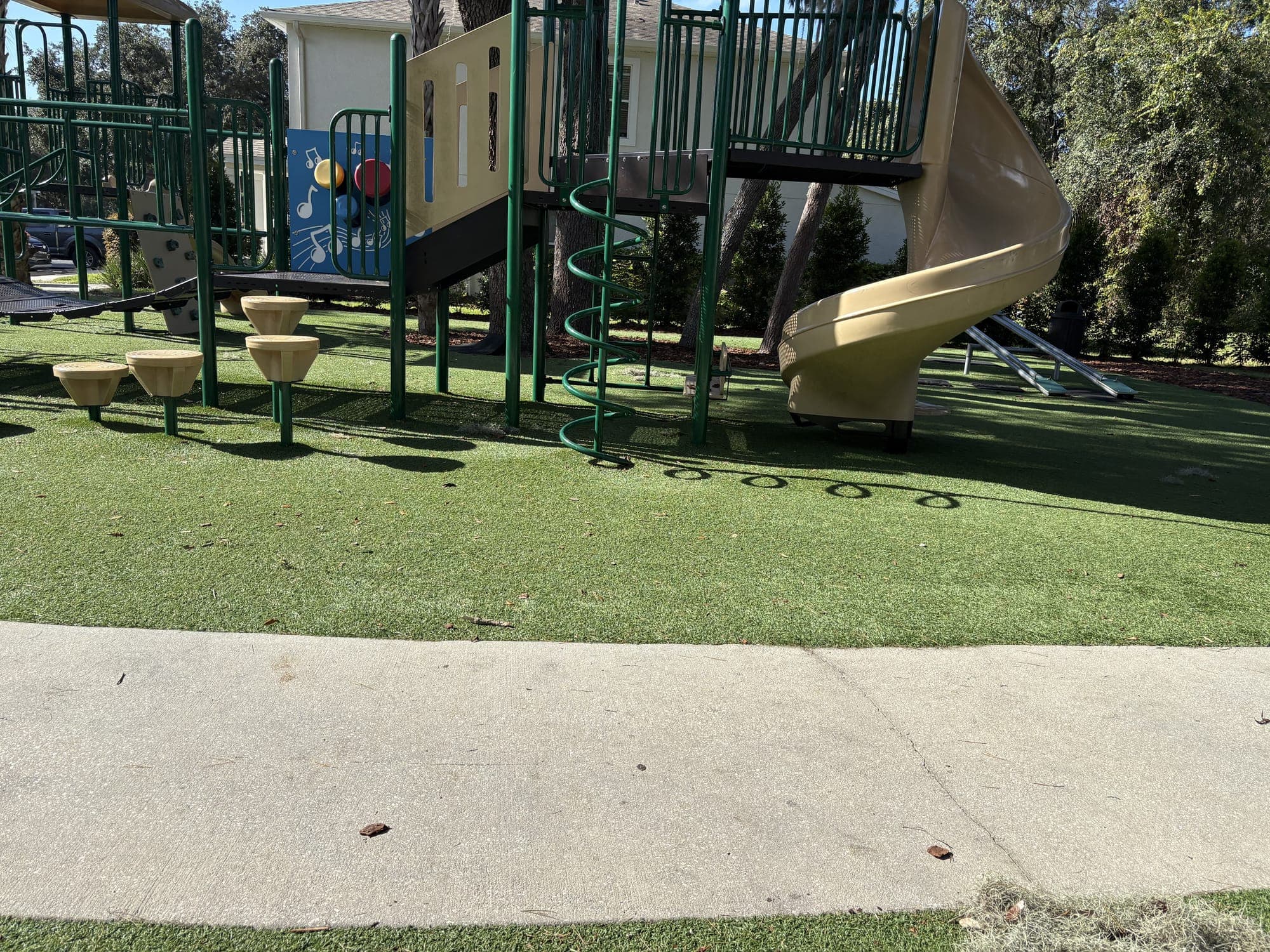 The view from the bench: the path, the turf, and the playground with stepping stumps and a tall slide.