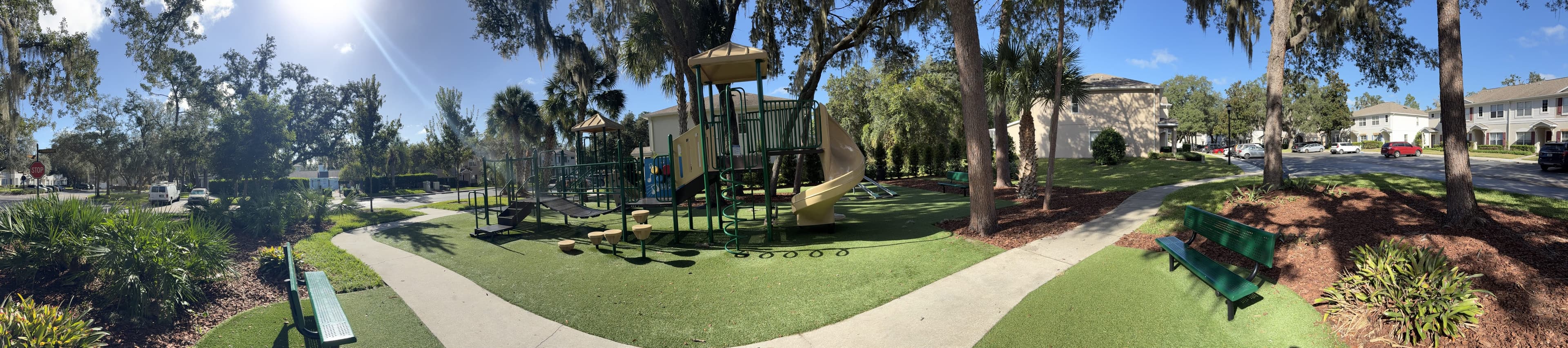 Panorama from the bench: the playground in the middle with a curving path around it, oaks and palms, the second bench on the right.