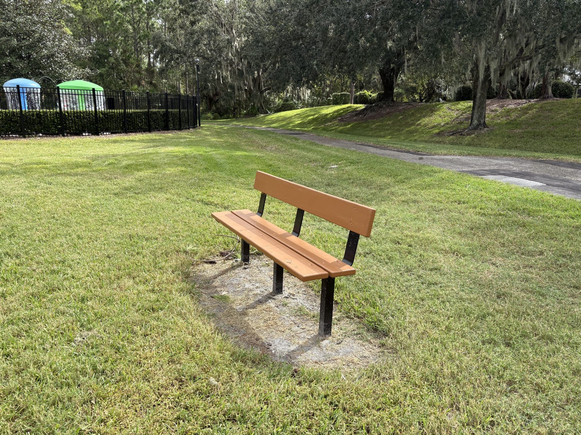 The bench on the lawn, with the pool fence on the left and a path under mossy oaks behind.
