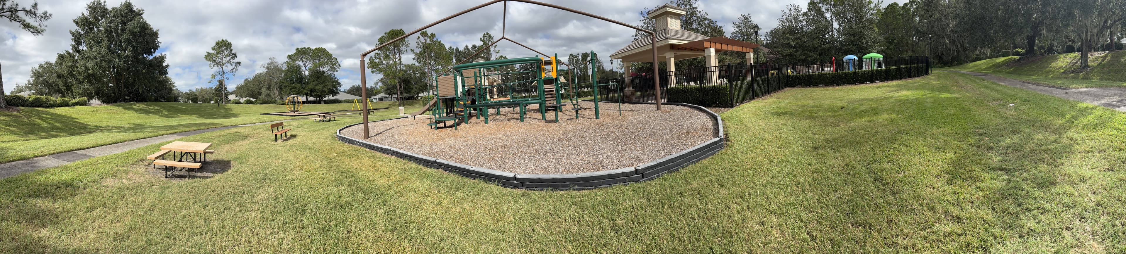 Panorama from the bench: lawn and picnic tables on the left, the playground and pavilion, a path heading off under oaks.