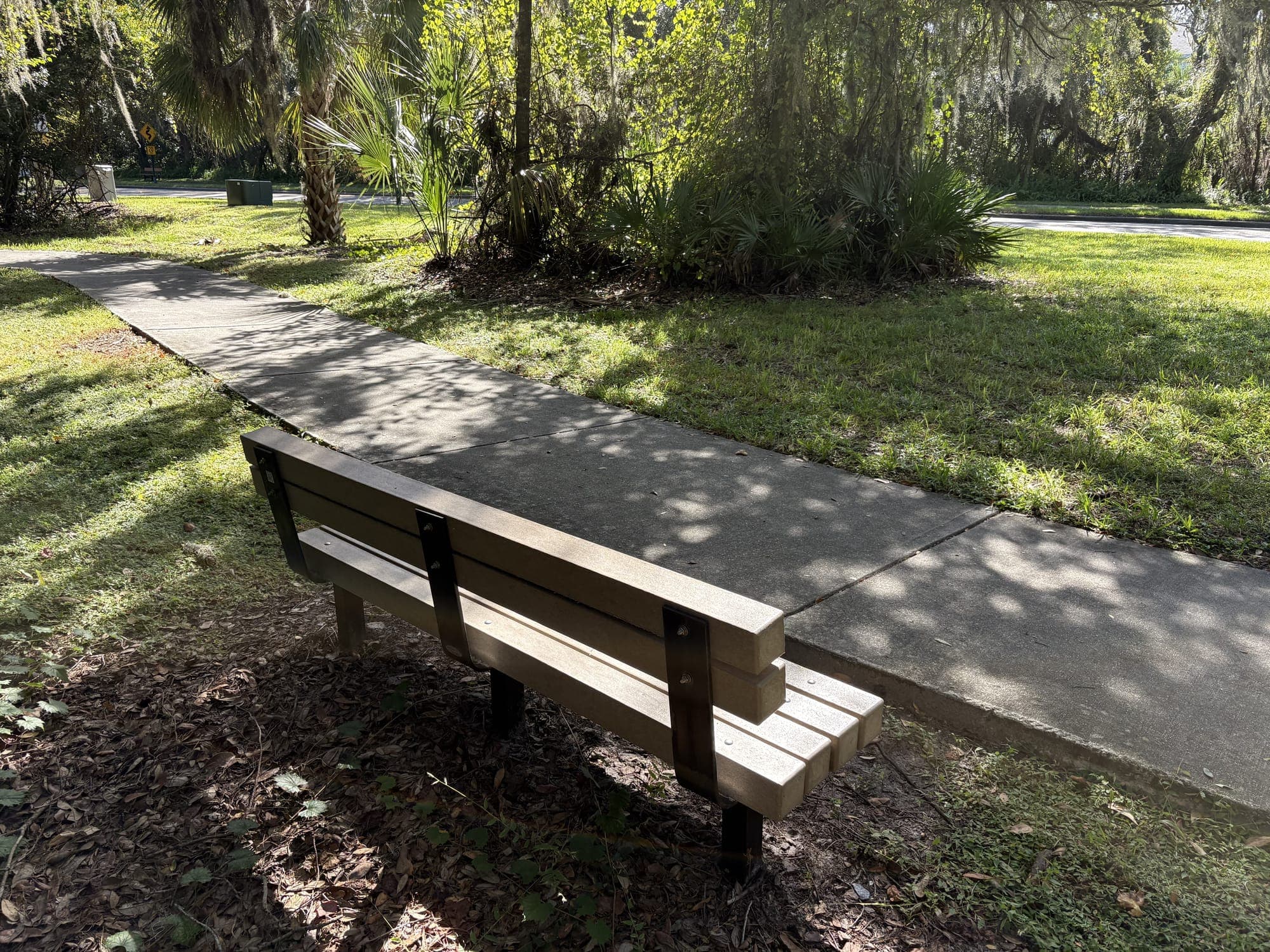 Side view of the bench at the edge of the path with trees and lawn behind.