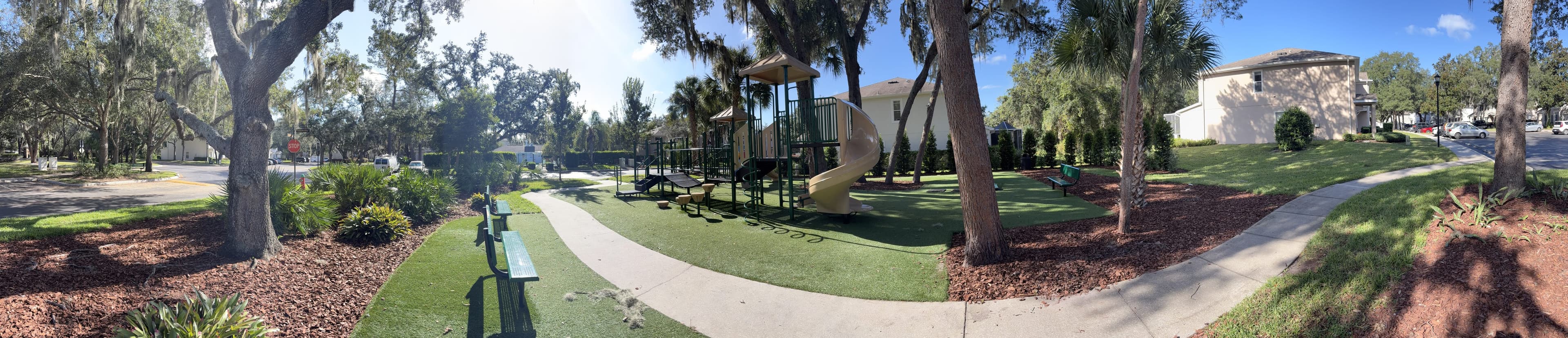 Panorama from the bench: a big oak and the street on the left, the playground in the middle, a house on the right.