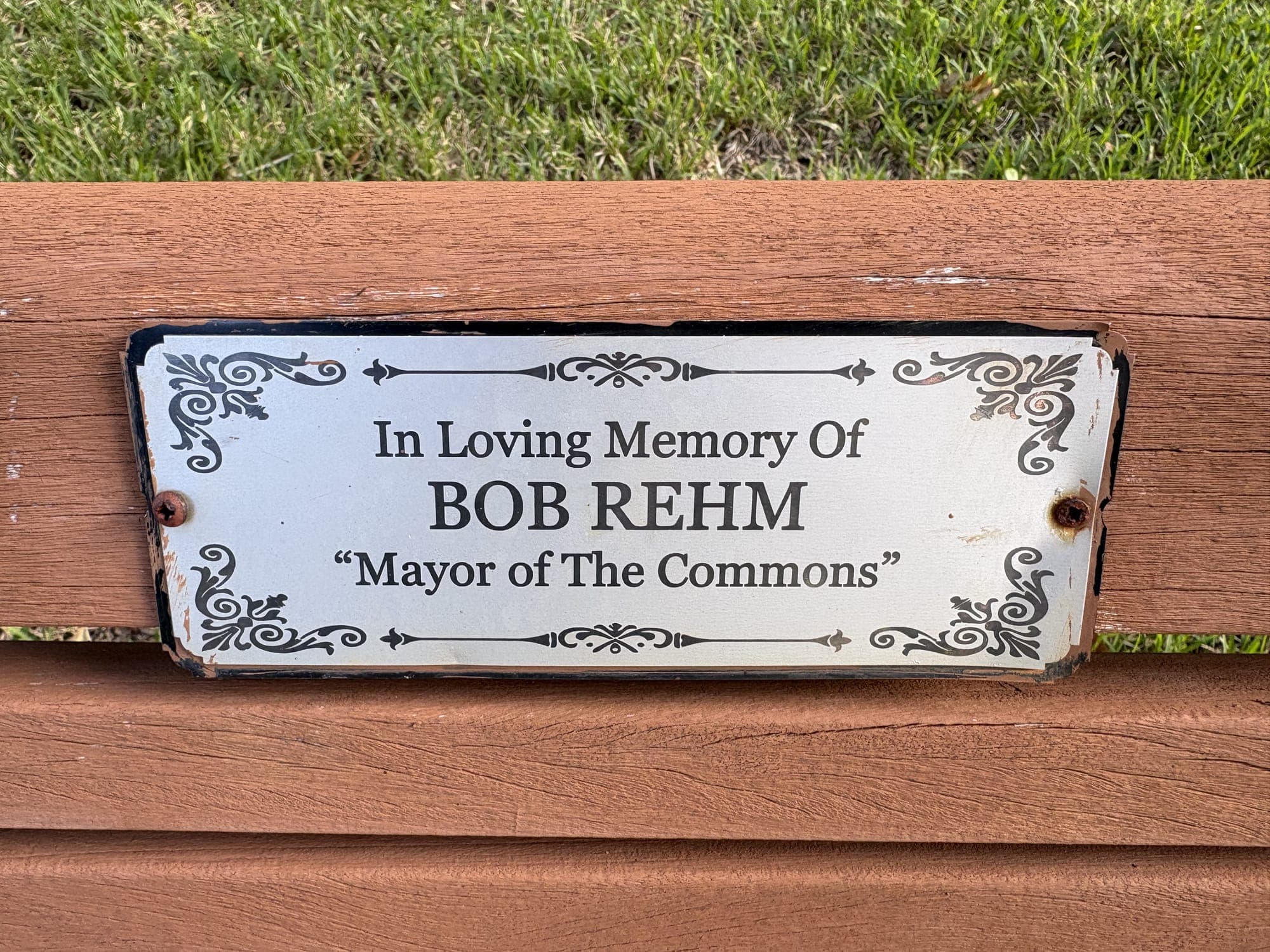 A small plaque on the bench: “In Loving Memory Of Bob Rehm, Mayor of The Commons.”
