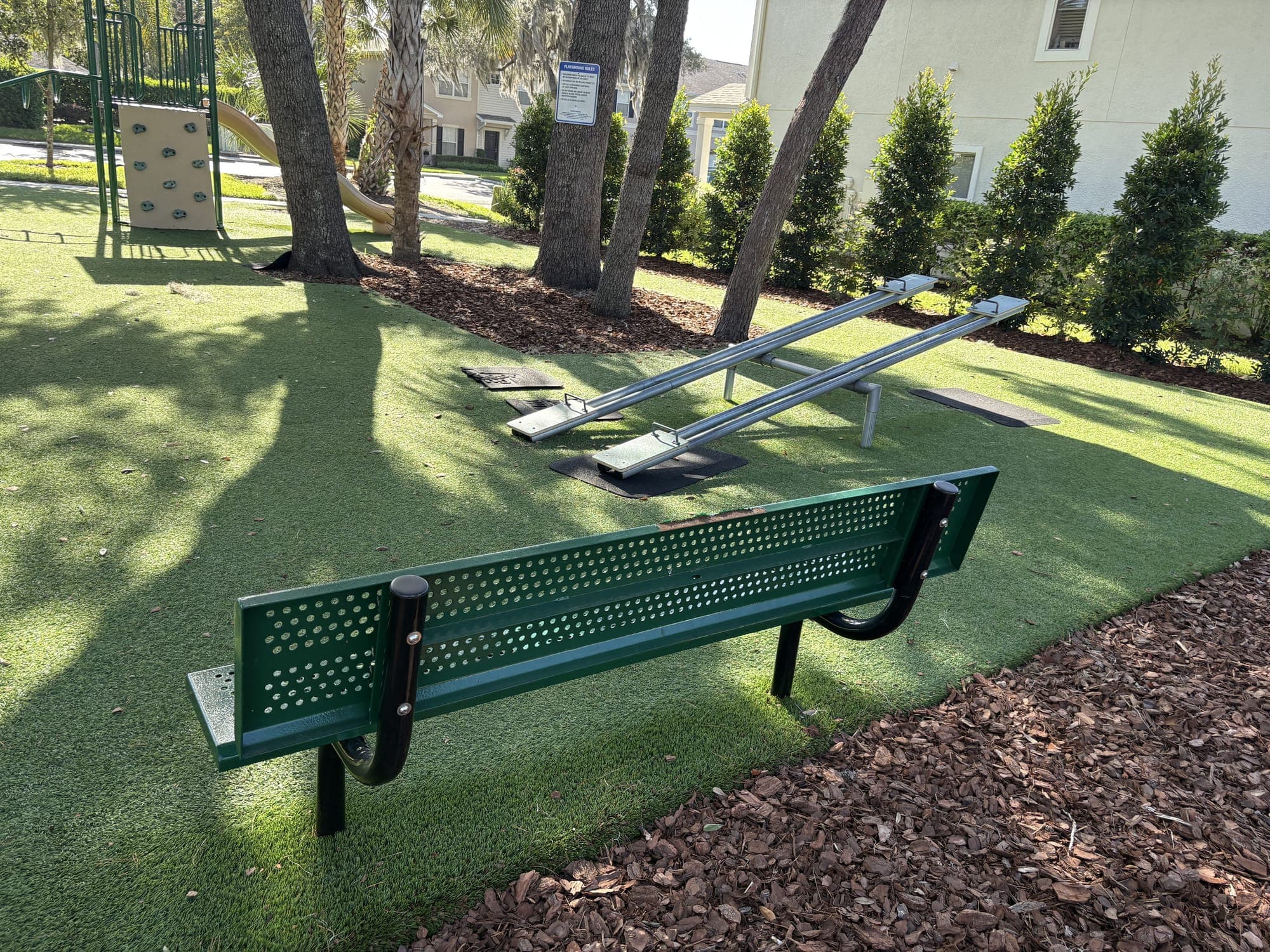 The bench from behind, looking toward the seesaws and a row of hedges.