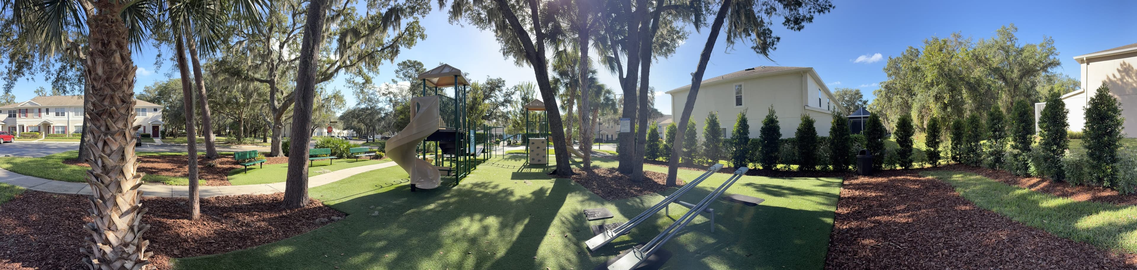Panorama from the bench: palms and oaks on the left, the playground and seesaws in the middle, houses on the right.