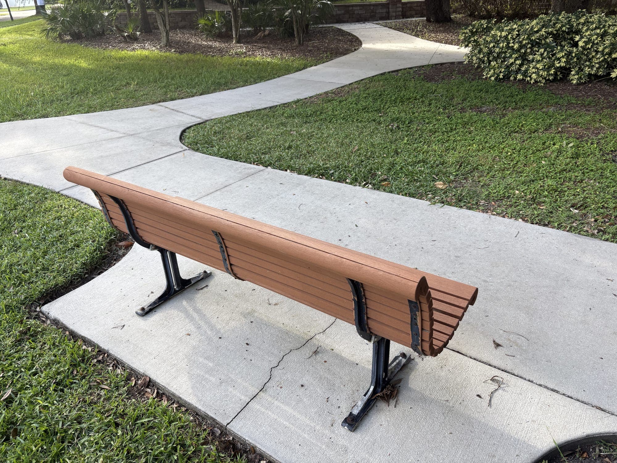 The bench from behind, beside a sidewalk that winds off between lawns.
